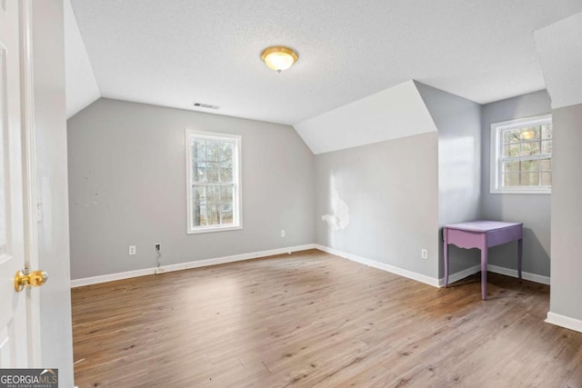 bonus room with a textured ceiling, light hardwood / wood-style flooring, vaulted ceiling, and plenty of natural light