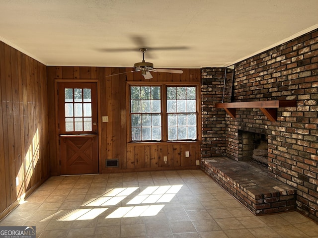 unfurnished living room featuring ceiling fan, wood walls, ornamental molding, and a brick fireplace