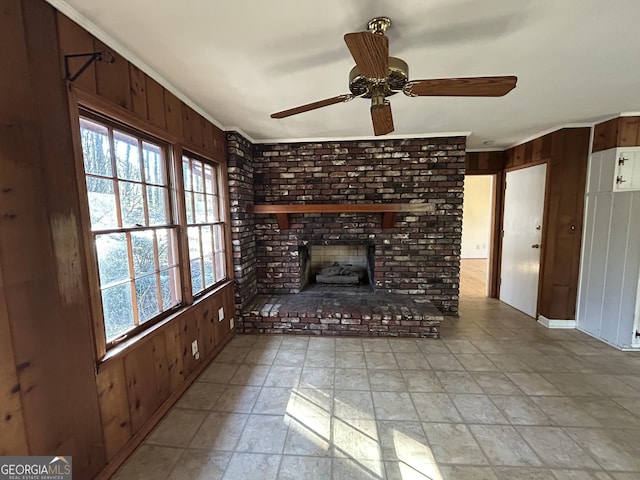 unfurnished living room featuring wooden walls, a brick fireplace, ceiling fan, and ornamental molding