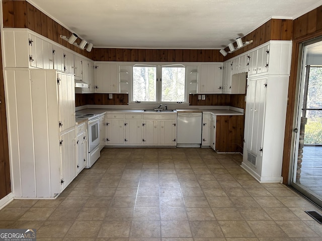 kitchen with wood walls, white appliances, sink, ornamental molding, and white cabinetry