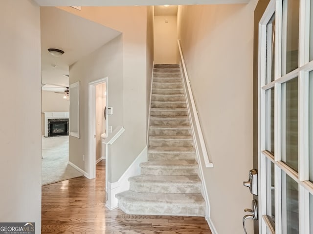 stairway featuring a fireplace, hardwood / wood-style flooring, and ceiling fan