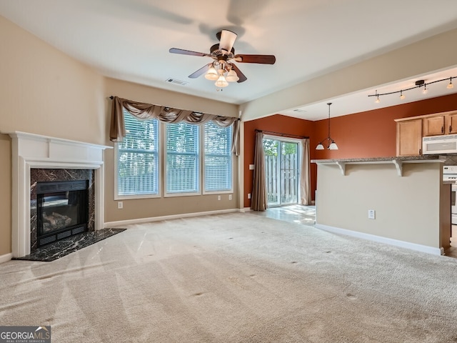 unfurnished living room with ceiling fan, a fireplace, rail lighting, and light carpet