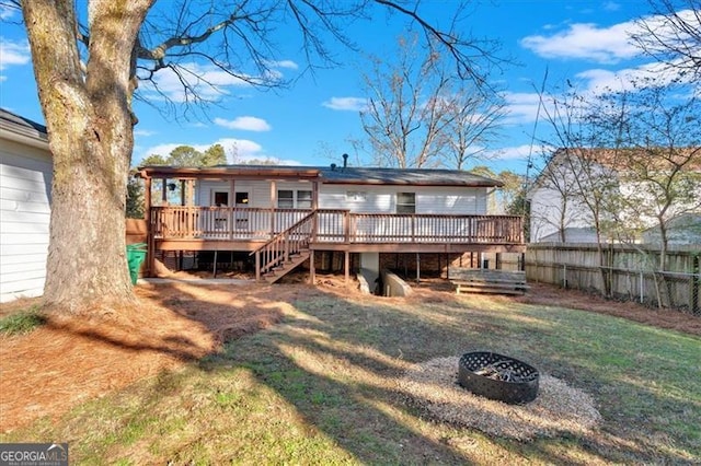 back of property with a wooden deck, a yard, and a fire pit