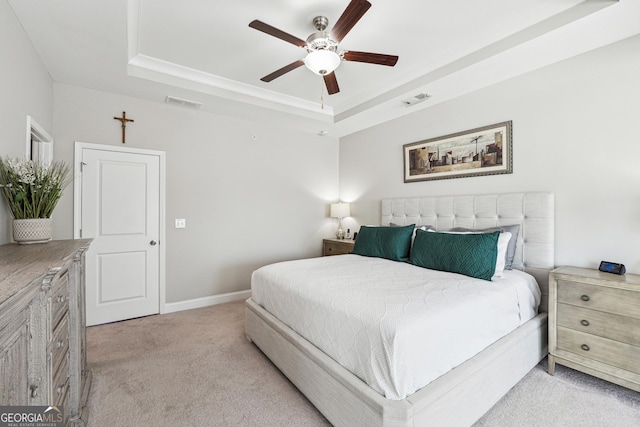 bedroom featuring ceiling fan, ornamental molding, light carpet, and a tray ceiling