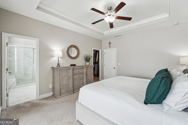 bedroom featuring a spacious closet, ensuite bathroom, light carpet, ceiling fan, and a tray ceiling