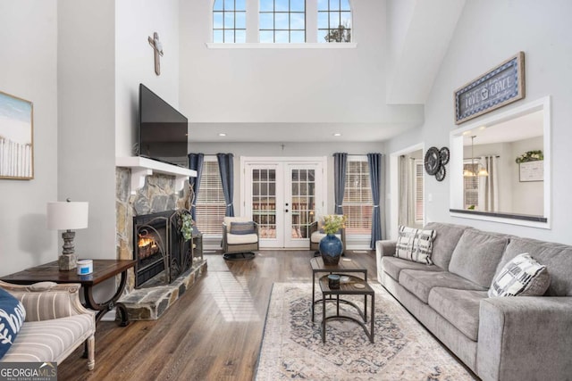 living room with dark hardwood / wood-style floors, a stone fireplace, a towering ceiling, and french doors