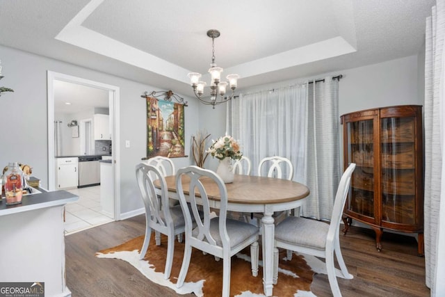 dining room featuring a chandelier, light hardwood / wood-style floors, a textured ceiling, and a tray ceiling