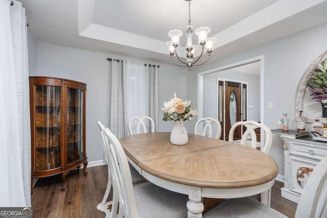 dining room featuring a tray ceiling, dark wood-type flooring, and an inviting chandelier