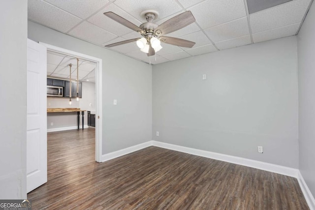 unfurnished room with a drop ceiling, ceiling fan, and dark hardwood / wood-style flooring