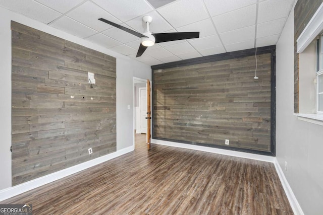 spare room with a paneled ceiling, wooden walls, ceiling fan, and wood-type flooring