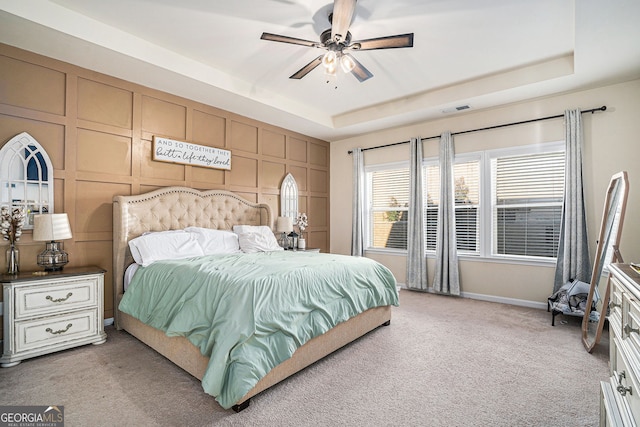 bedroom featuring visible vents, light carpet, a decorative wall, a raised ceiling, and ceiling fan