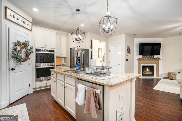 kitchen with light stone countertops, dark wood finished floors, open floor plan, a lit fireplace, and appliances with stainless steel finishes