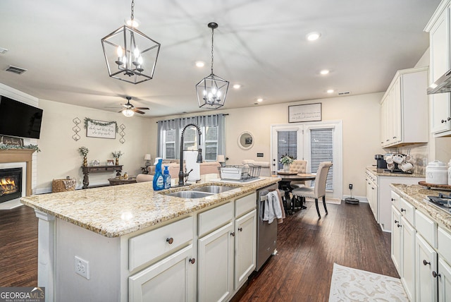 kitchen with visible vents, a sink, stainless steel dishwasher, a warm lit fireplace, and dark wood finished floors