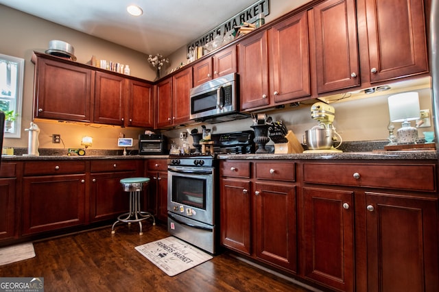 kitchen with dark hardwood / wood-style flooring, appliances with stainless steel finishes, and dark stone counters