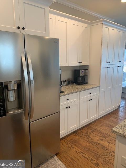 kitchen with light stone countertops, stainless steel fridge with ice dispenser, hardwood / wood-style flooring, and white cabinetry