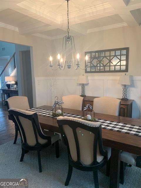 dining space featuring beamed ceiling, ornamental molding, a notable chandelier, and hardwood / wood-style floors