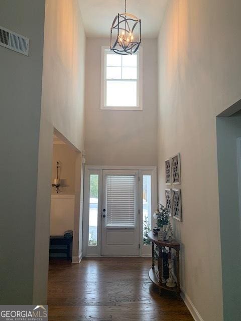 foyer entrance with dark hardwood / wood-style flooring, a towering ceiling, and a chandelier