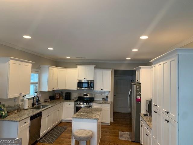 kitchen with white cabinets, appliances with stainless steel finishes, a kitchen island, and sink