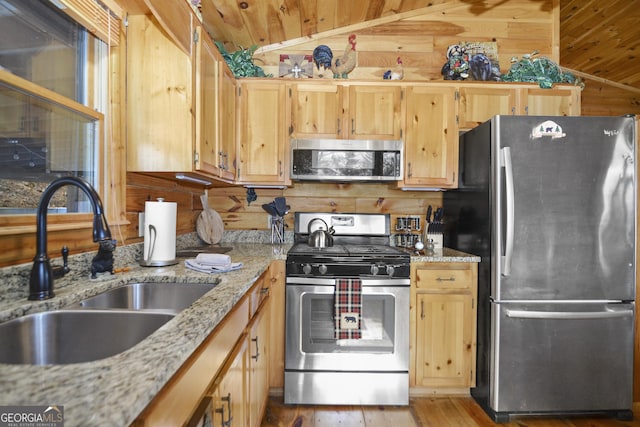 kitchen with light stone counters, stainless steel appliances, wooden walls, sink, and light hardwood / wood-style flooring