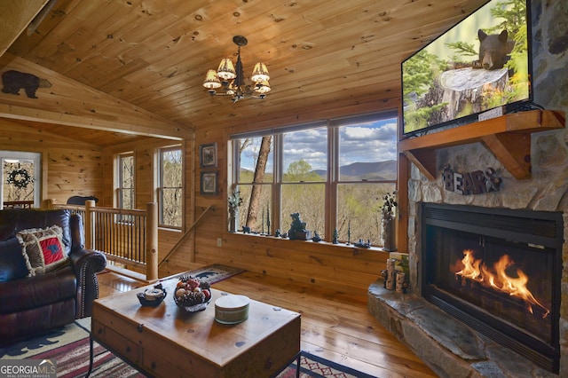 living room with an inviting chandelier, a stone fireplace, vaulted ceiling, wooden walls, and hardwood / wood-style flooring