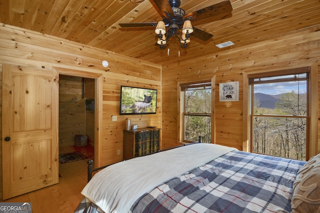 bedroom featuring light wood-type flooring, wood ceiling, ceiling fan, multiple windows, and wood walls