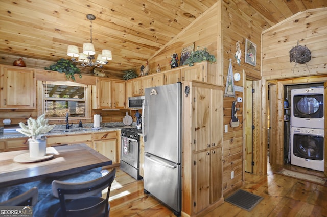 kitchen featuring light brown cabinetry, hanging light fixtures, stacked washer / drying machine, and appliances with stainless steel finishes