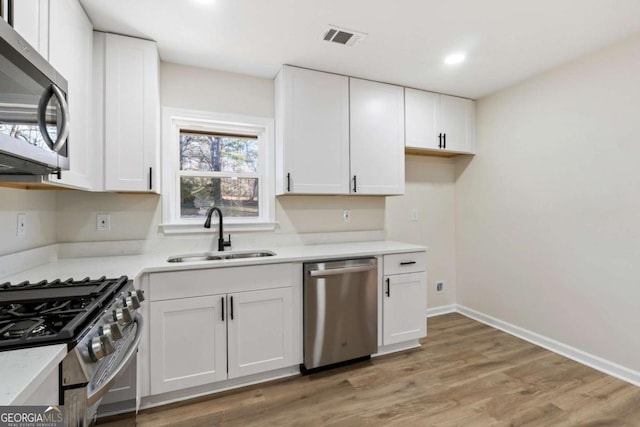 kitchen with white cabinetry, sink, appliances with stainless steel finishes, and light hardwood / wood-style flooring