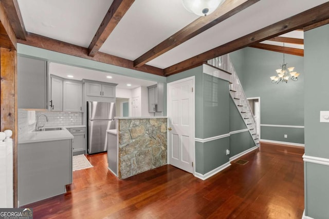 kitchen with an inviting chandelier, stainless steel fridge, backsplash, dark wood-type flooring, and sink