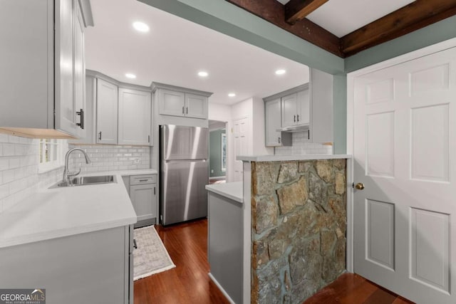 kitchen with backsplash, sink, dark wood-type flooring, stainless steel refrigerator, and beamed ceiling