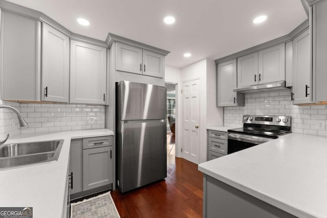 kitchen with appliances with stainless steel finishes, dark hardwood / wood-style flooring, decorative backsplash, sink, and gray cabinets