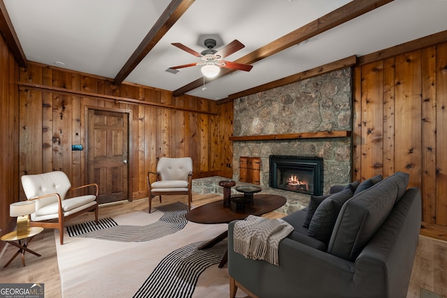 interior space featuring beamed ceiling, a fireplace, light hardwood / wood-style floors, wood walls, and ceiling fan