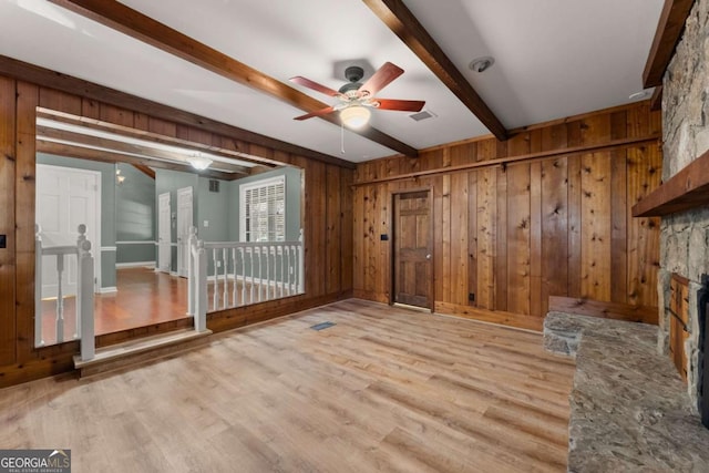 interior space featuring ceiling fan, light hardwood / wood-style floors, a stone fireplace, and beamed ceiling