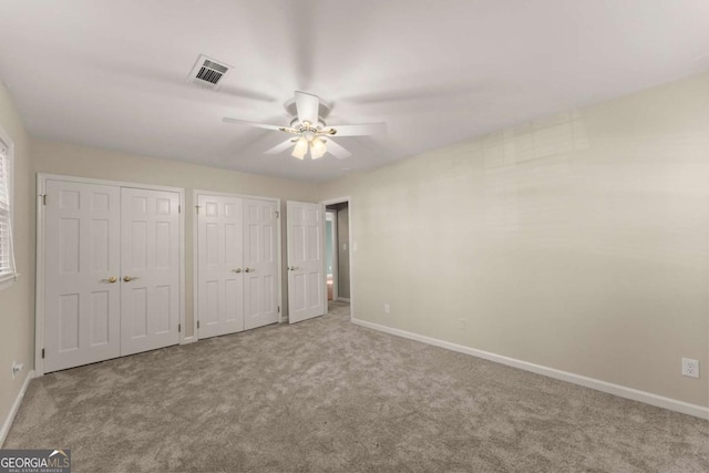 unfurnished bedroom featuring ceiling fan, light colored carpet, and multiple closets