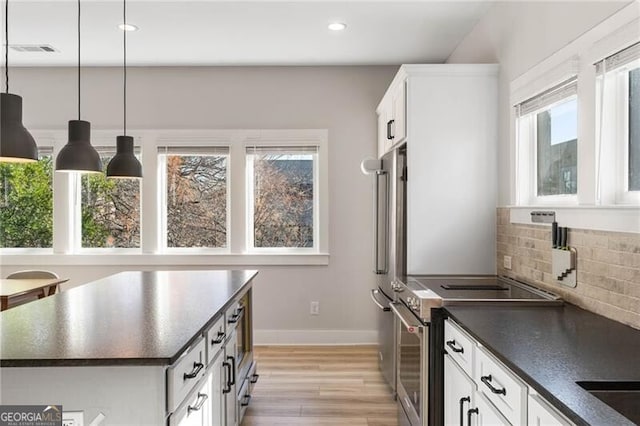 kitchen featuring light hardwood / wood-style flooring, hanging light fixtures, backsplash, white cabinets, and high end stove