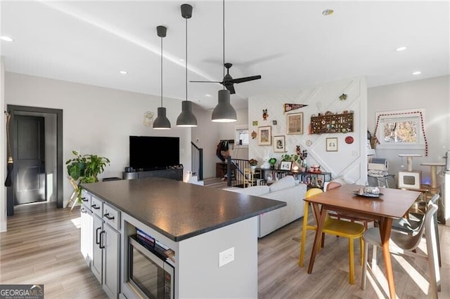 kitchen with white cabinetry, ceiling fan, stainless steel microwave, light hardwood / wood-style flooring, and decorative light fixtures