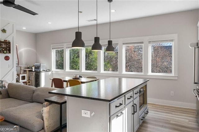 kitchen featuring decorative light fixtures, light hardwood / wood-style floors, built in microwave, ceiling fan, and a kitchen breakfast bar