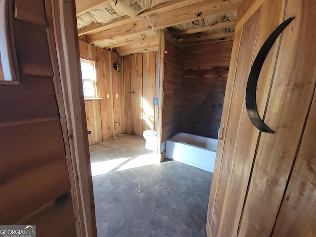 bathroom featuring toilet, a bathing tub, and wood walls