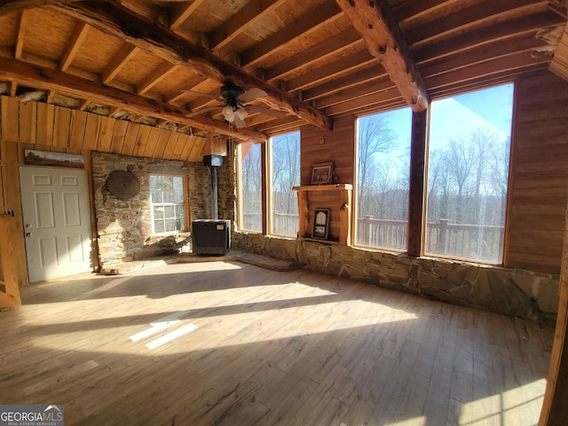 unfurnished living room featuring ceiling fan, hardwood / wood-style floors, beamed ceiling, a wood stove, and wooden ceiling