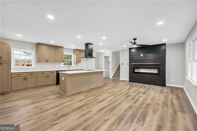 kitchen featuring dishwasher, a center island, wall chimney exhaust hood, light hardwood / wood-style floors, and a large fireplace