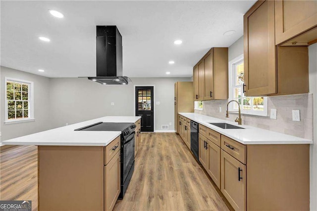 kitchen featuring sink, wall chimney exhaust hood, a healthy amount of sunlight, light hardwood / wood-style floors, and black appliances