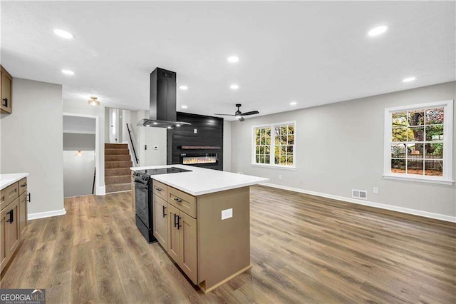 kitchen with dark hardwood / wood-style flooring, black range with electric cooktop, island range hood, a center island, and plenty of natural light