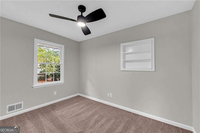 spare room featuring built in shelves, ceiling fan, and carpet