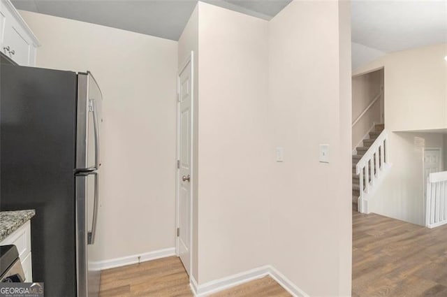 kitchen featuring light stone countertops, white cabinetry, stainless steel refrigerator, and light hardwood / wood-style flooring