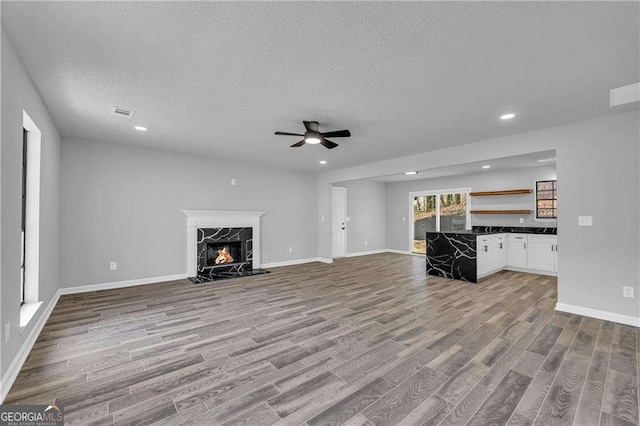 unfurnished living room with light wood-type flooring, a textured ceiling, ceiling fan, and a premium fireplace