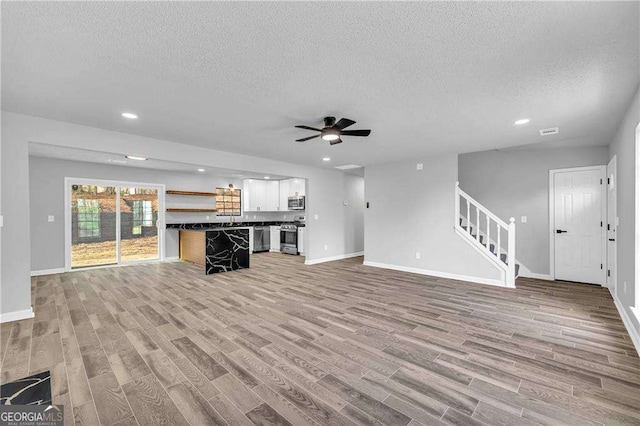 unfurnished living room featuring ceiling fan, light hardwood / wood-style floors, and a textured ceiling