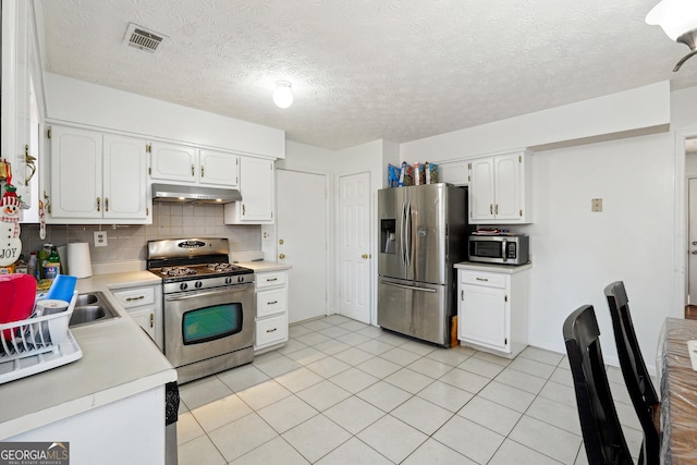 kitchen featuring a textured ceiling, appliances with stainless steel finishes, tasteful backsplash, light tile patterned flooring, and white cabinetry