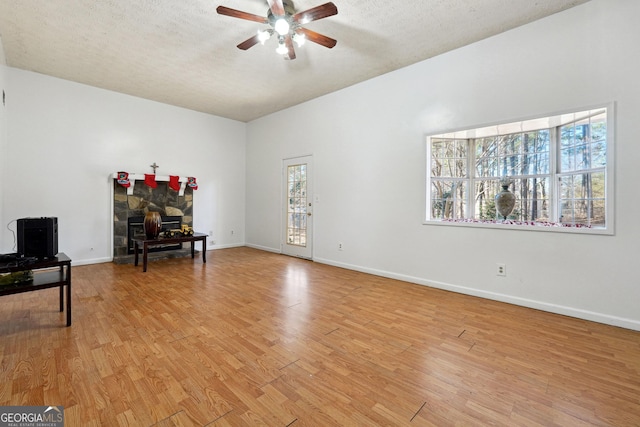 interior space featuring a fireplace, a textured ceiling, light hardwood / wood-style floors, and ceiling fan