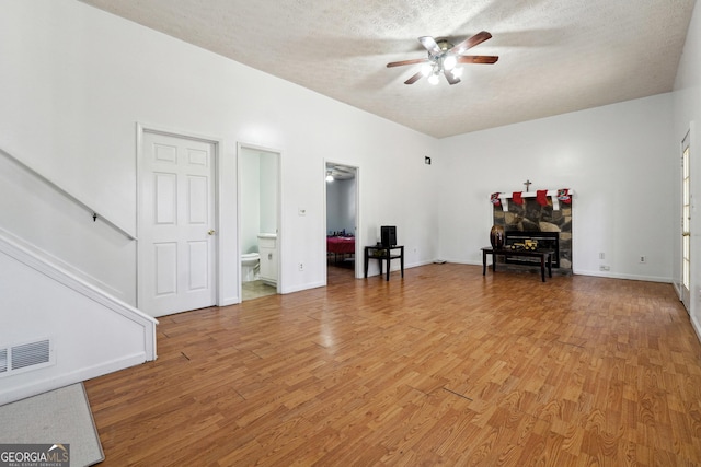 interior space featuring ceiling fan, a stone fireplace, wood-type flooring, and a textured ceiling