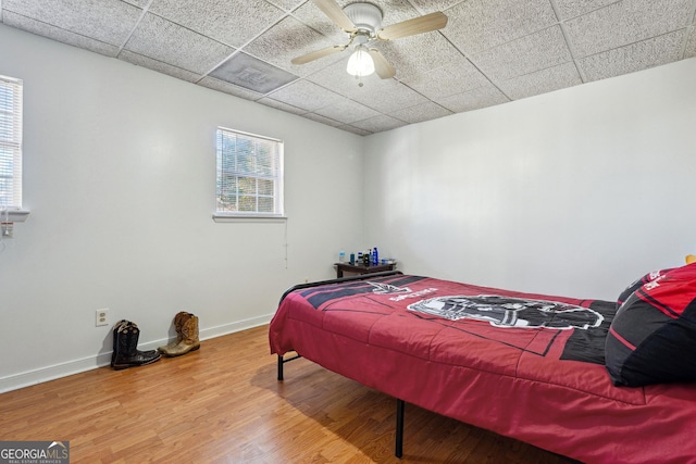 bedroom featuring wood-type flooring, a drop ceiling, and ceiling fan