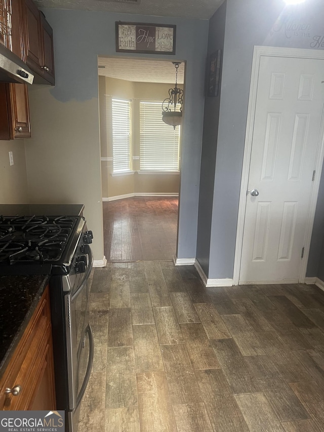 kitchen with extractor fan, dark hardwood / wood-style floors, dark stone counters, and gas range